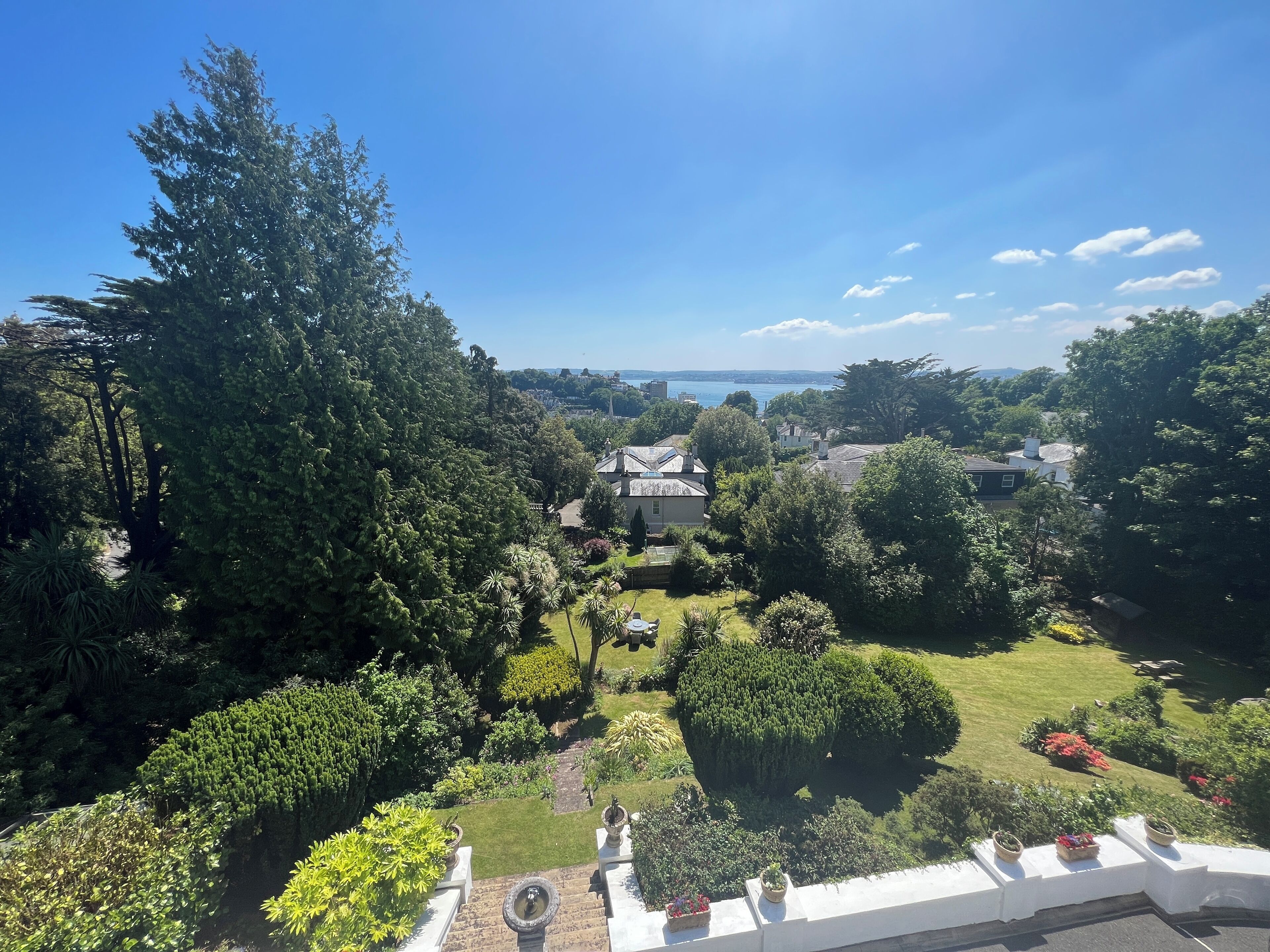 A residential area with a well-maintained garden, a large tree, and a view of the sea.