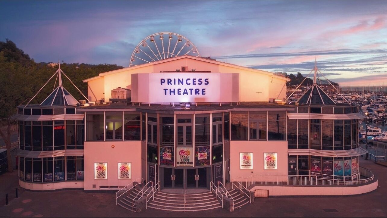 A Princess Theatre with a large marquee, glass entrance, and a Ferris wheel in the background.
