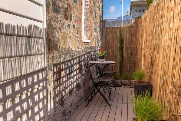 Une petite terrasse extérieure avec une table et des chaises, une clôture en bambou et un mur en pierre.