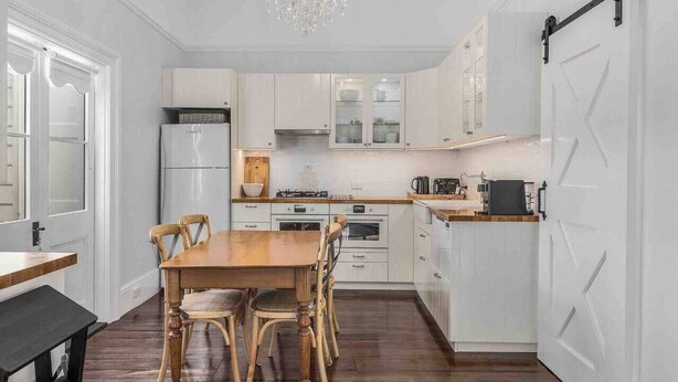 A modern kitchen with white cabinets, a wooden dining table, and a chandelier.
