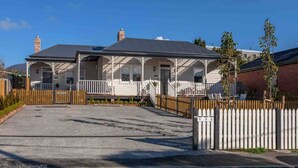 A two-story house with a porch, a fenced driveway, and a gate labeled with numbers.