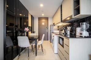 A modern kitchen with a dining area, featuring a refrigerator, stove, and various appliances. - The Panora apartments by NLA (Choeng Thale)