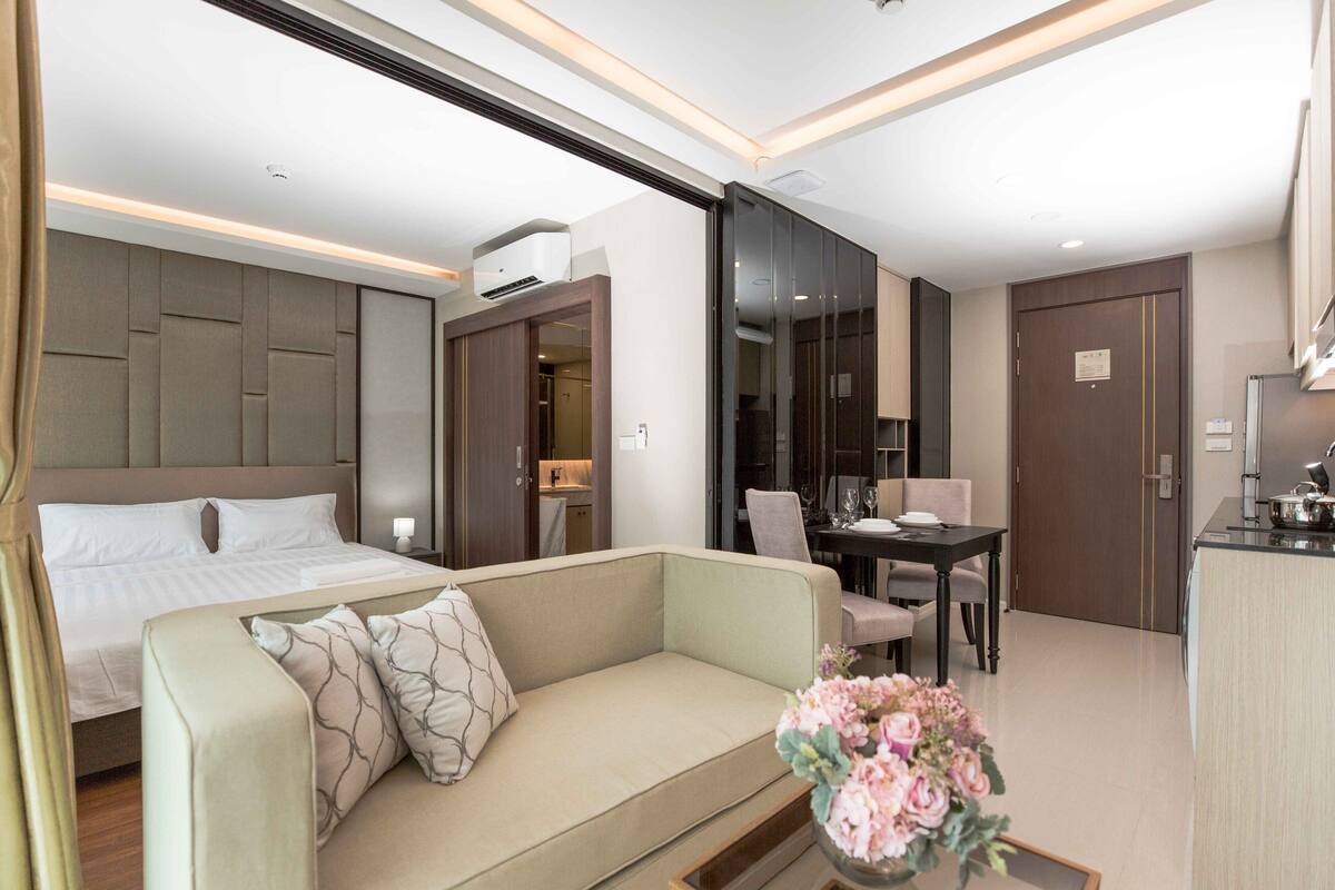 A modern hotel room with a bed, a sofa, a dining area, and a kitchenette.