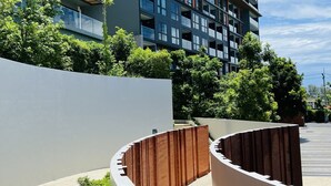 A modern multi-story building with balconies, surrounded by greenery and a curved pathway. - The Panora apartments by NLA (Choeng Thale)