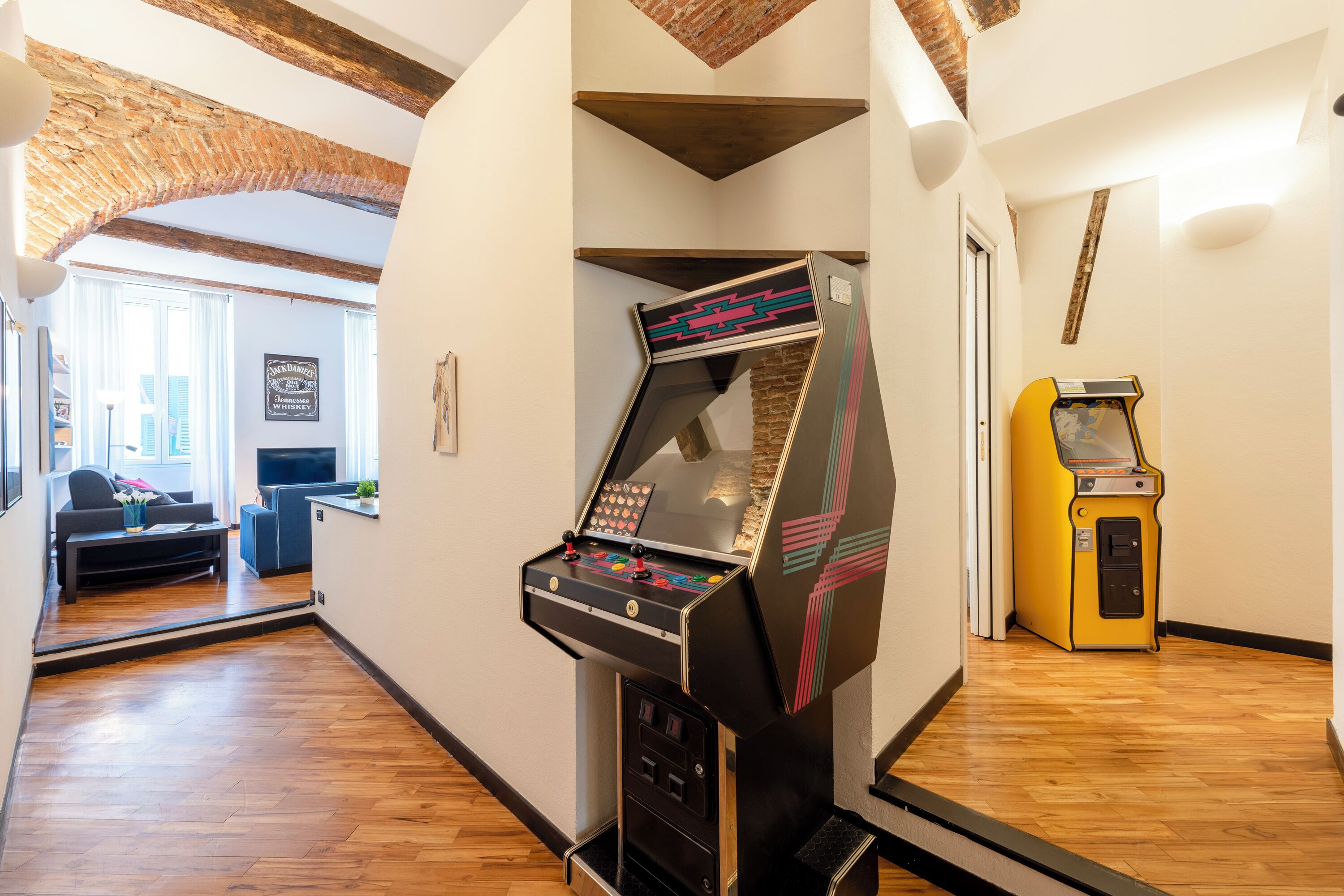 A room with a wooden floor, a gaming machine, a sofa, and a television.