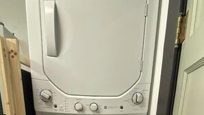 Un appareil compact, blanc, combinant une machine à laver et un sèche-linge à chargement frontal, doté de boutons de commande et d’une poignée de porte.