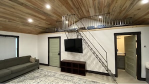 Un salon moderne avec un plafond en bois, un escalier, un téléviseur à écran plat, un canapé et un tapis à motifs.