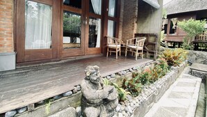 Una casa de madera con un porche, una estatua de piedra y un jardín con plantas tropicales.