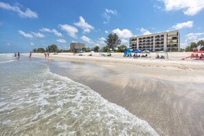 A beach with a hotel in the background, clear skies, and people on the sand.