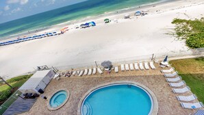 A swimming pool area with a view of the beach, lounge chairs, and umbrellas.