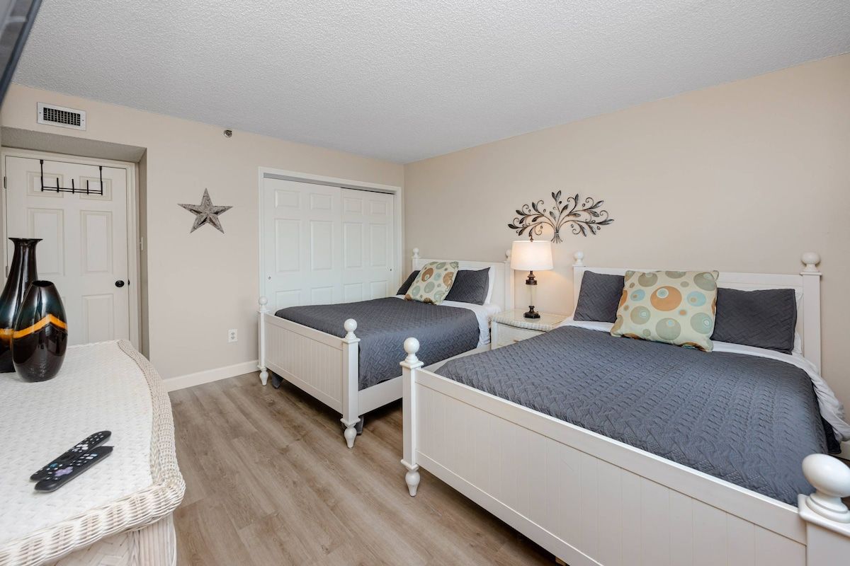 A bedroom with two beds, a bedside table with a lamp, a star decoration on the wall, and a door with a towel rack.