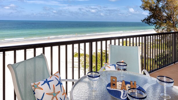 A balcony with a glass table, chairs, and a view of the beach.