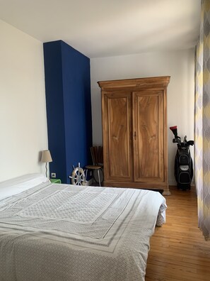Ein Schlafzimmer mit einem großen Bett, einem Holzschrank, einem Sessel, einem kleinen Tisch und einer Golftasche.