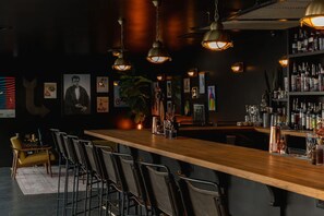 Zona bar con un lungo bancone, diverse lampade a sospensione e una varietà di bottiglie e bicchieri.