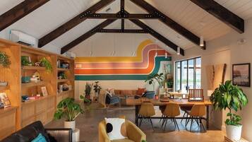 A spacious living area with a high ceiling, wooden beams, a colorful abstract wall, and a cozy seating arrangement.