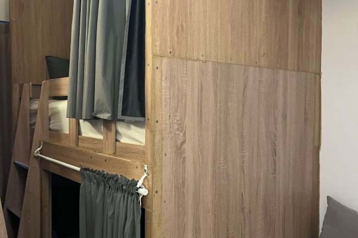 A bunk bed with curtains, a wooden wall, and a window.