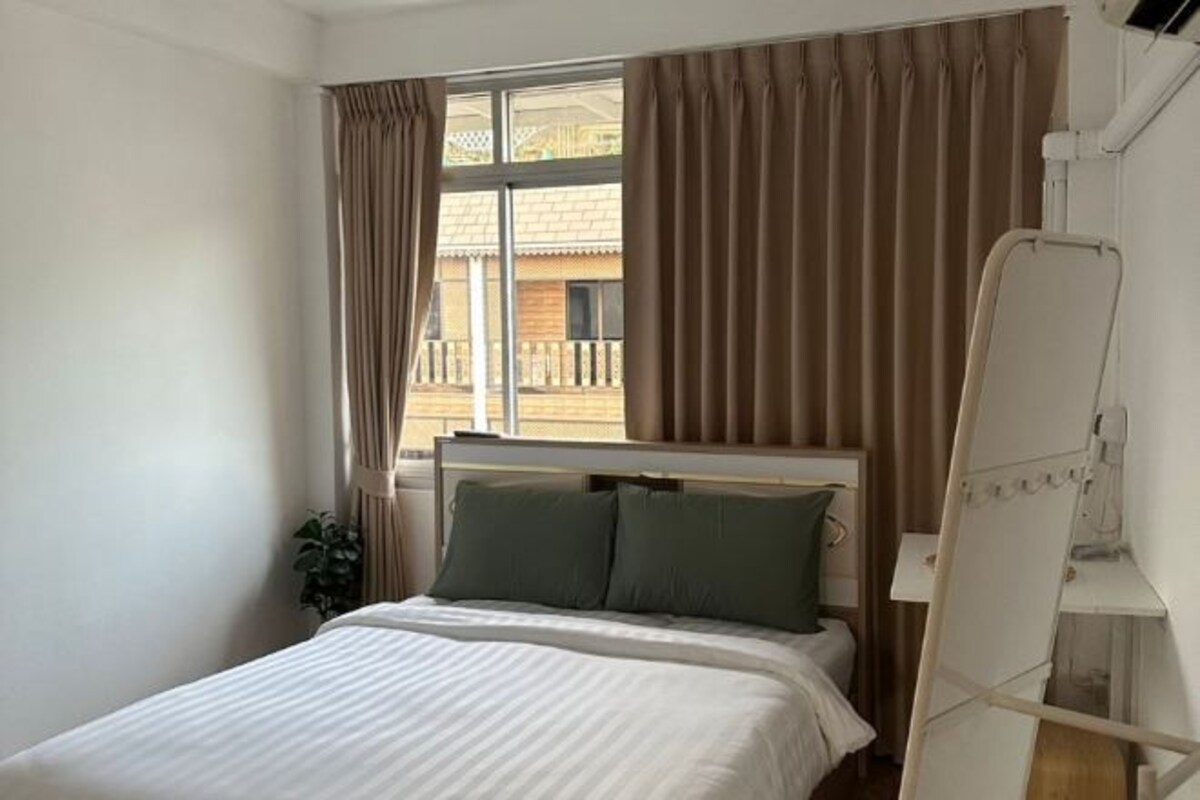 A bedroom with a bed, curtains, a window, and a white bedside table.