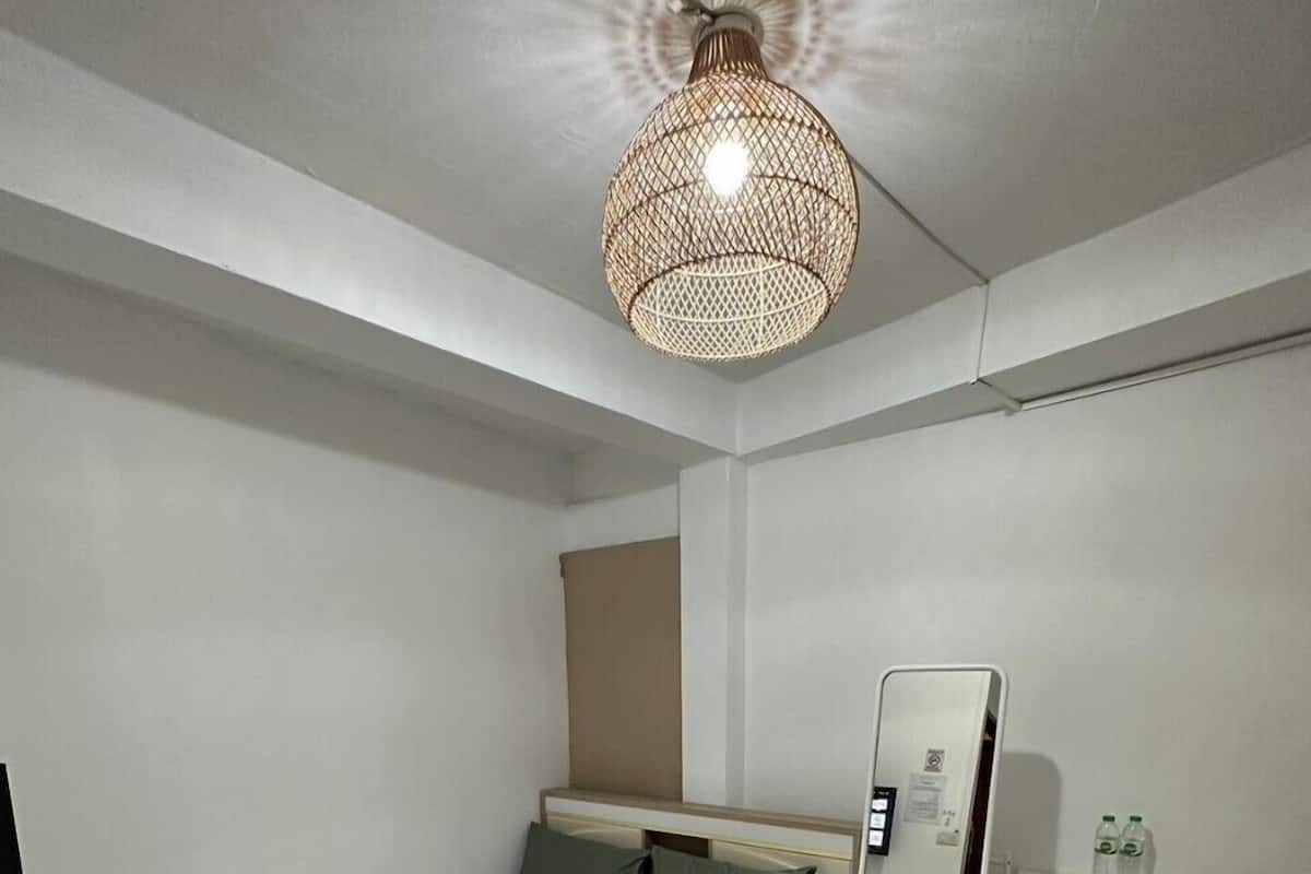 A modern hotel room with a neatly made bed, a bedside table with a mirror, a small desk, and a unique woven light fixture.