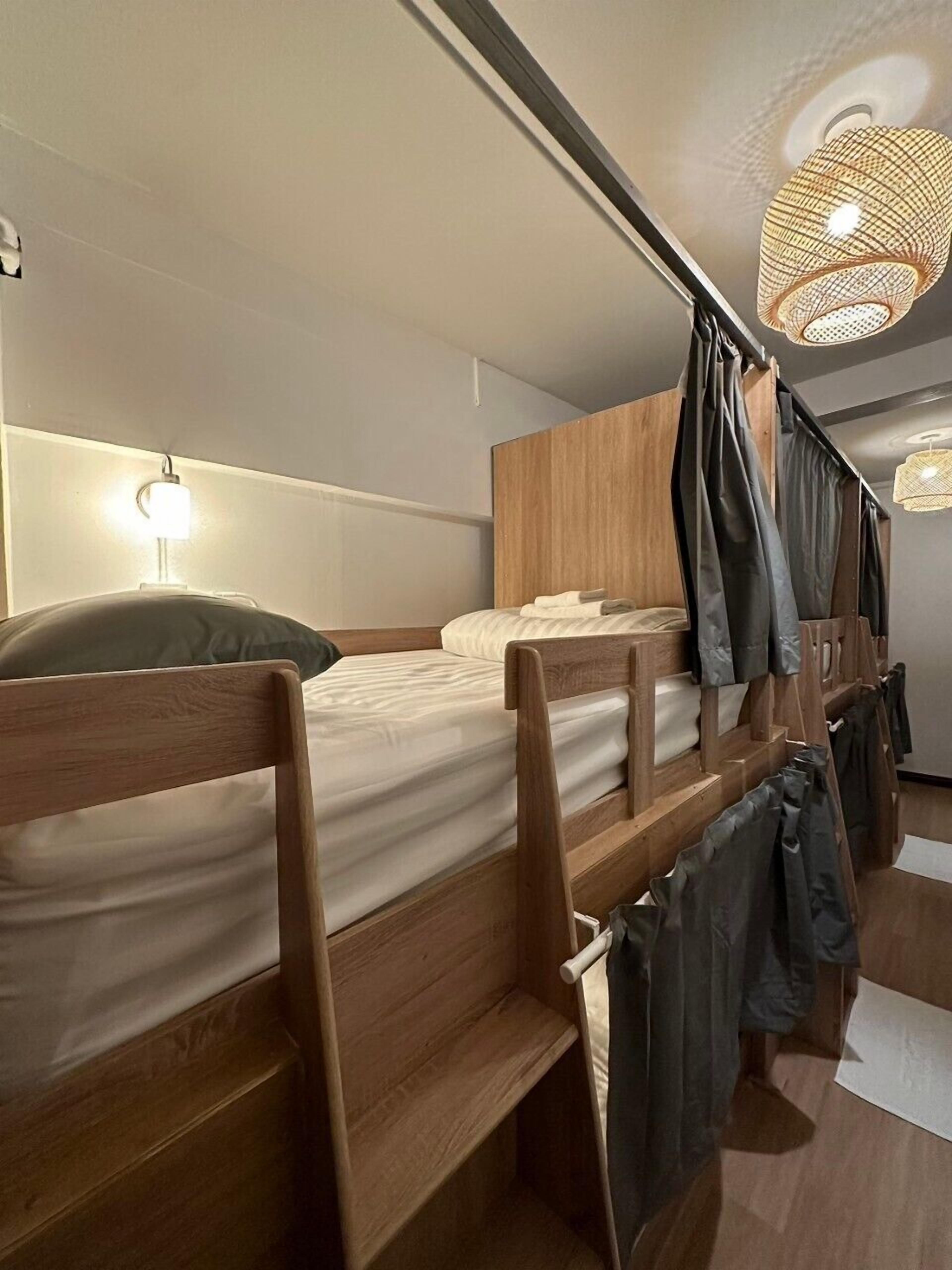 A modern, compact room with bunk beds, wooden headboards, and a hanging light fixture.