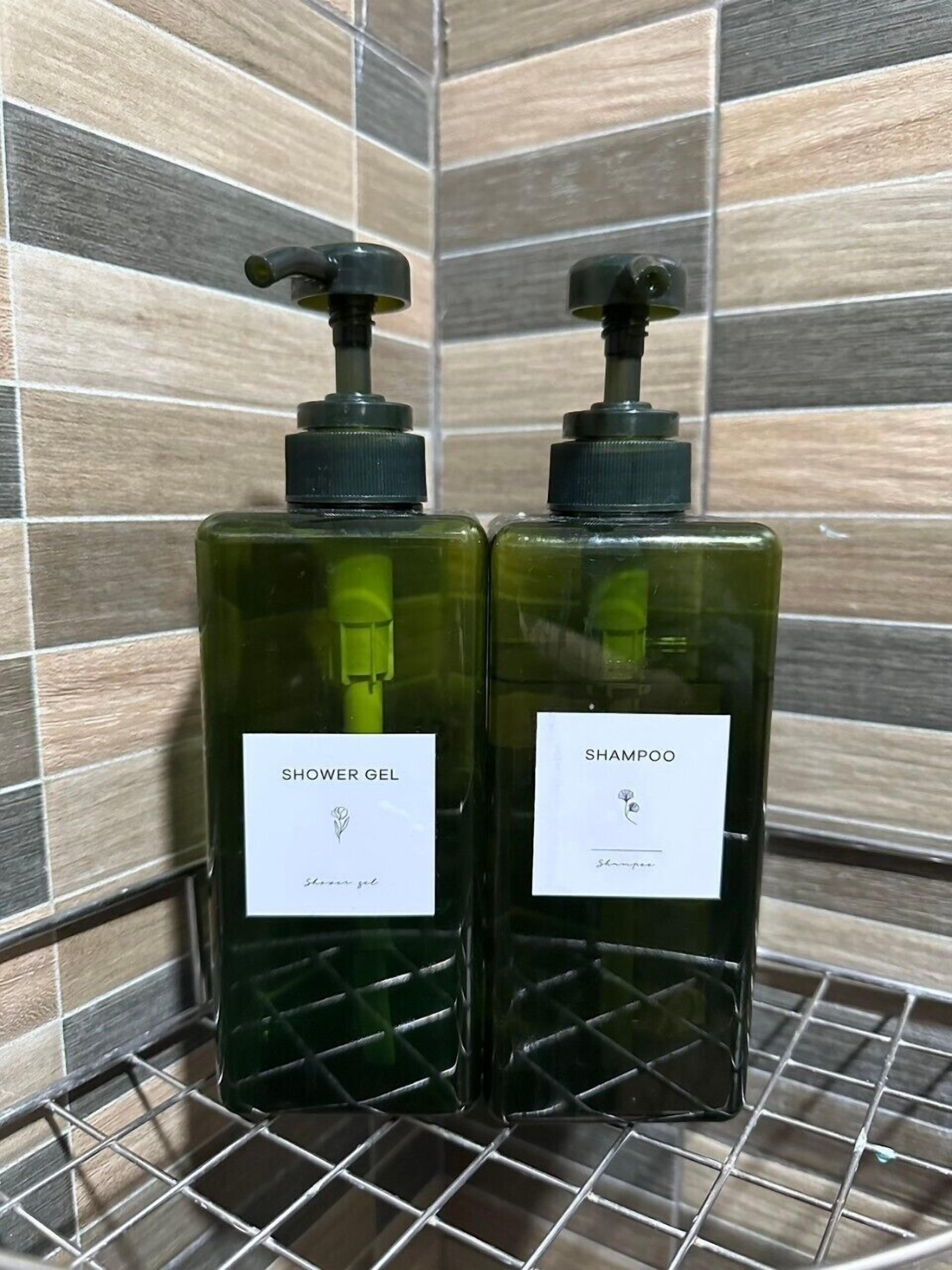 Dos botellas de gel de ducha y champú sobre una estantería metálica, frente a una pared de azulejos.