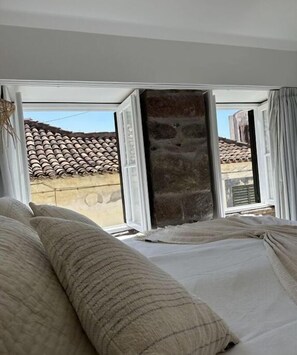 Ein Schlafzimmer mit einem großen Bett, einer Steinsäule und Blick auf ein Ziegeldach.