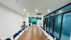Une salle de conférence avec une longue table en bois, des chaises bleues, un tableau blanc et un écran fixé au mur.