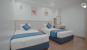 Habitación de hotel con dos camas, cada una con cabecera azul y almohada a juego. Un mesita de noche de madera se encuentra entre las camas, y una pequeña mesa de madera con un espejo y un estante encima.