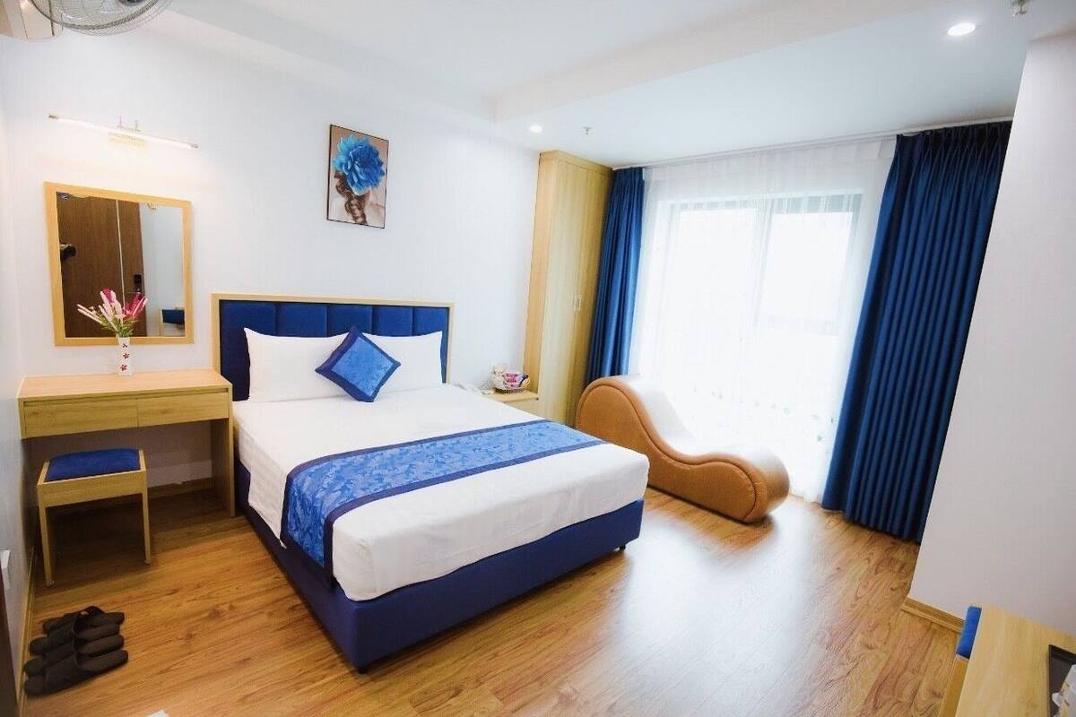 A hotel room with a bed, a desk, a chair, a mirror, and a window with curtains.