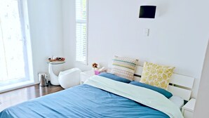 Une chambre moderne avec un grand lit, une petite table de chevet, une commode et une fenêtre avec des stores.