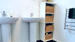 Une salle de bain avec deux lavabos blancs, un meuble blanc agrémenté de paniers en osier et un porte-serviettes.