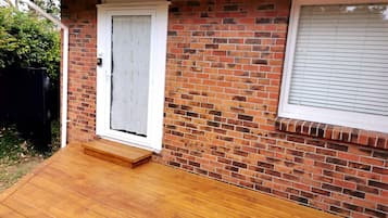 A brick house with a wooden deck, a white door, and a window with blinds.