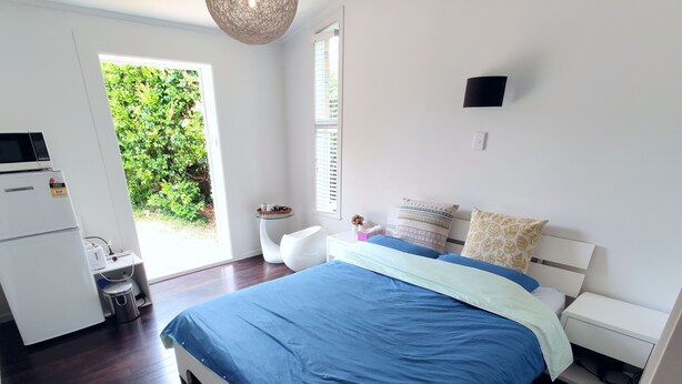 Une chambre moderne avec un grand lit, une petite table de chevet, une armoire blanche et un four à micro-ondes encastré.