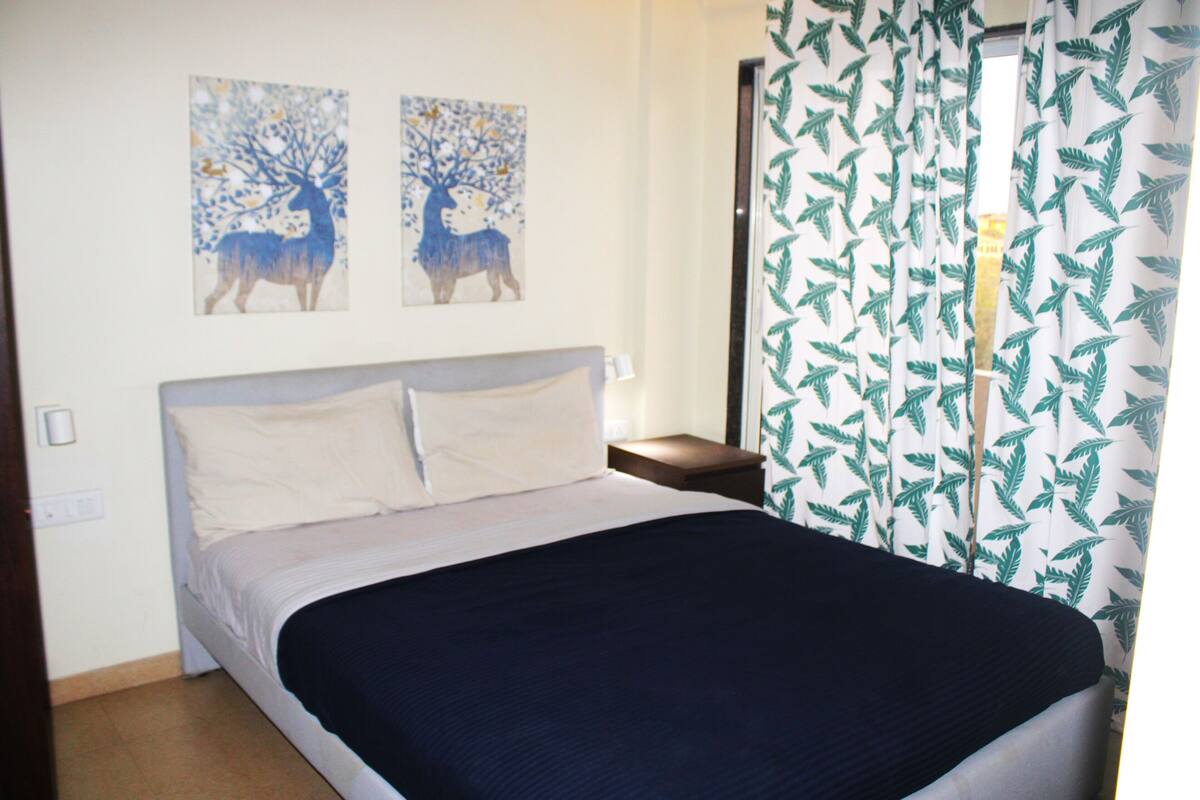 A bedroom with a bed, two wall art pieces, a nightstand, and curtains.