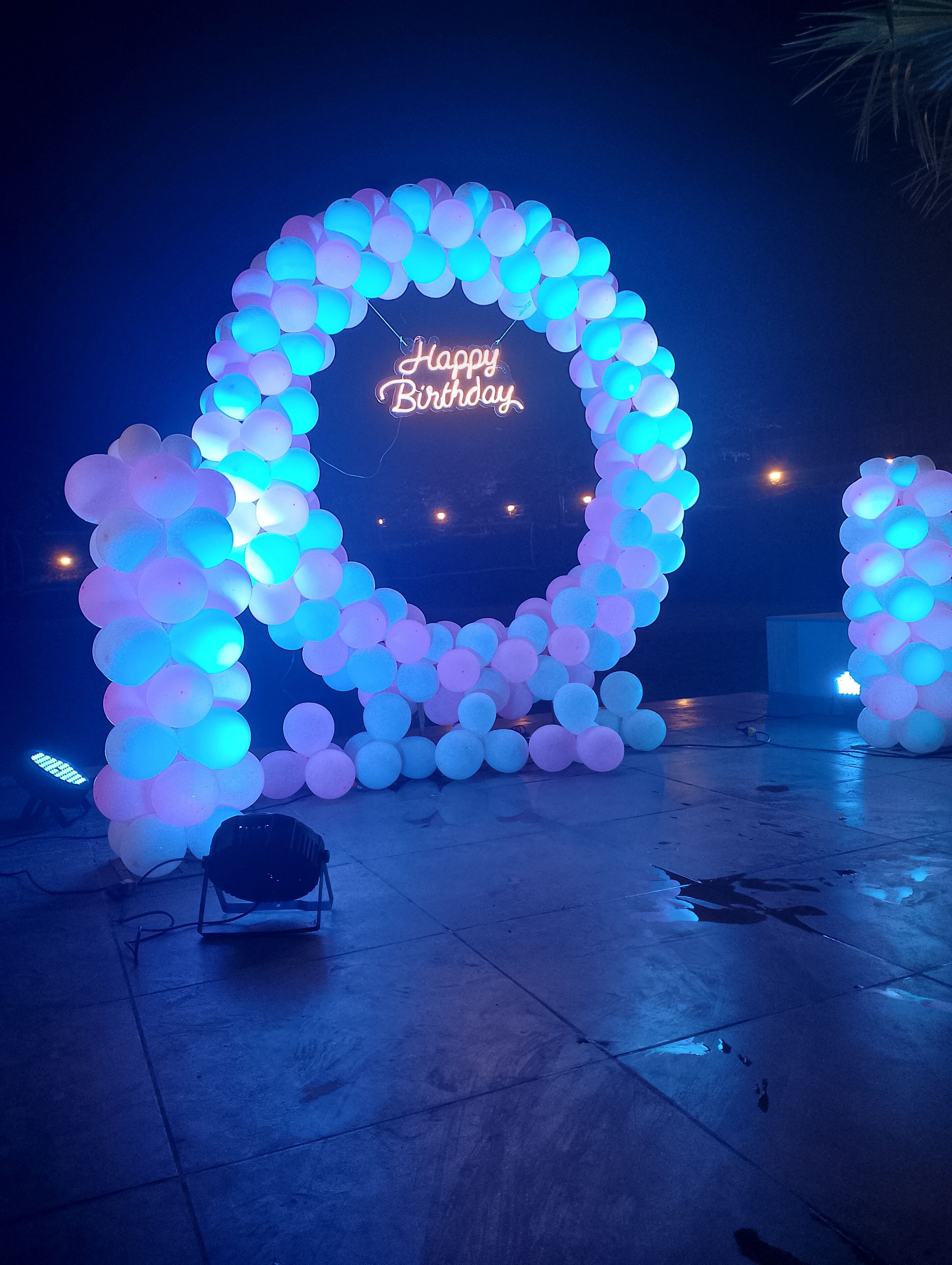 A neon 'Happy Birthday' sign surrounded by a circular arrangement of balloons.