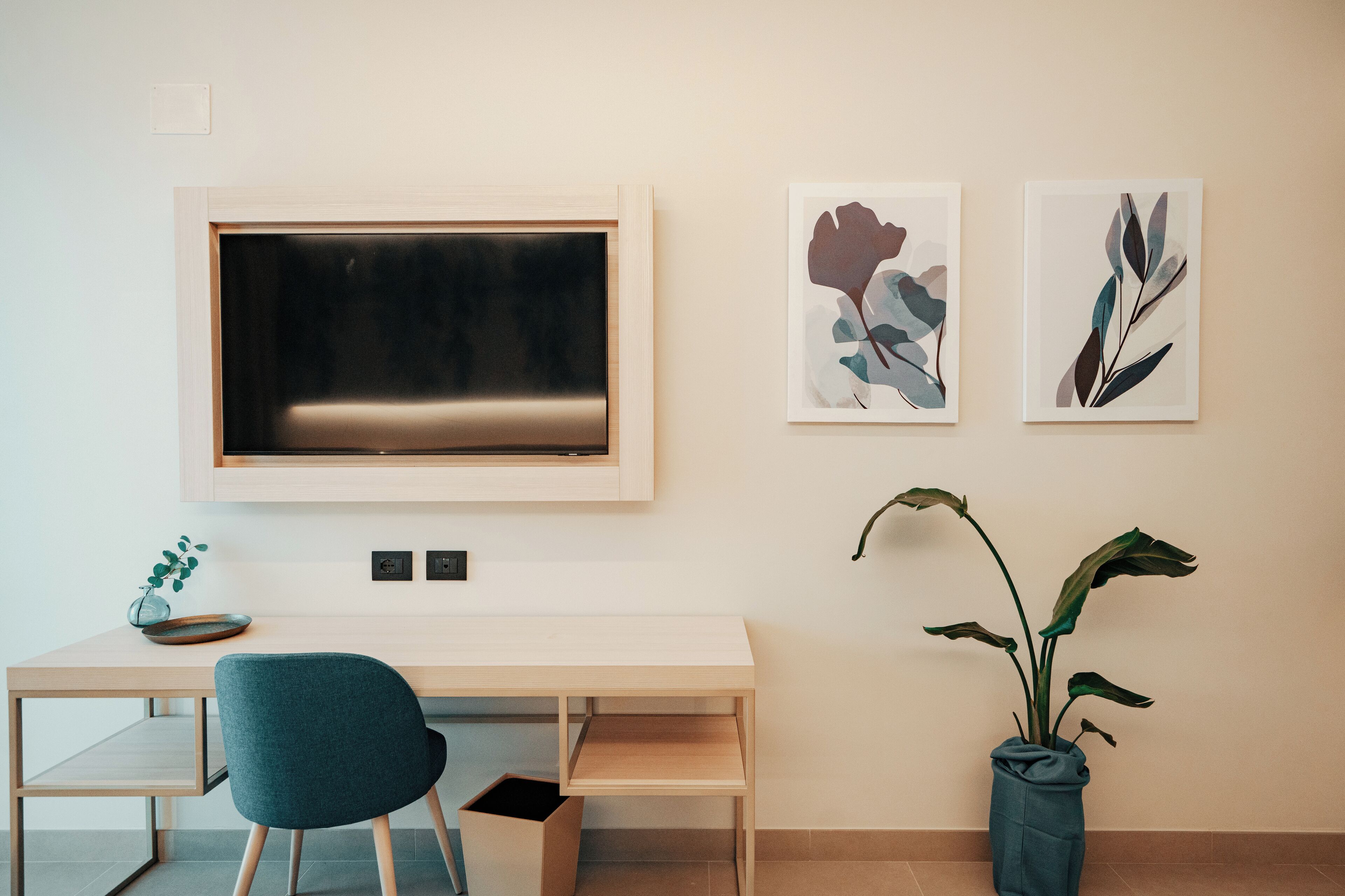 A modern room with a wooden desk, a blue chair, a large flat-screen TV, and two framed artworks on the wall.