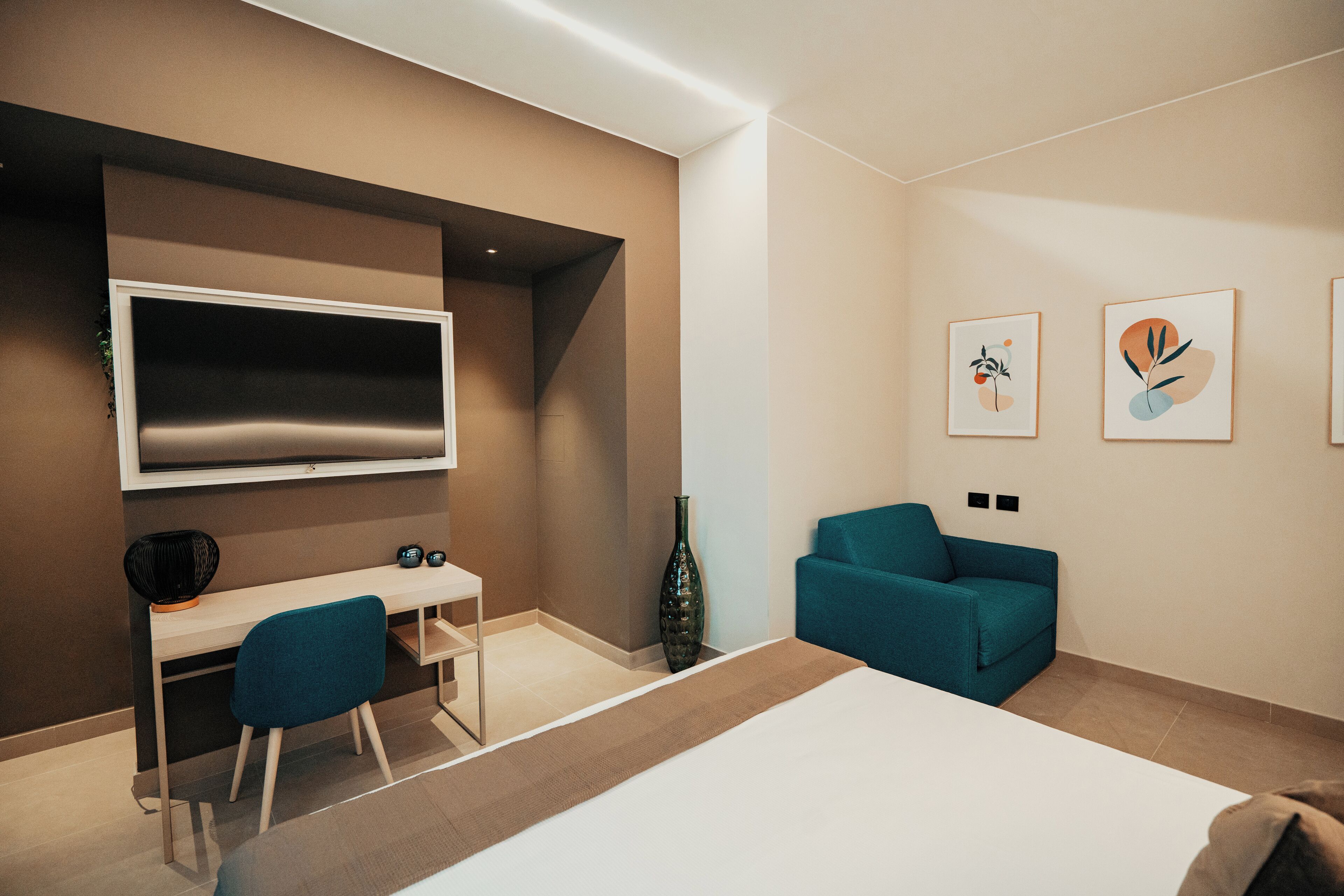 Quarto de hotel moderno com uma cama grande, uma mesa com cadeira, TV na parede e duas obras de arte emolduradas.