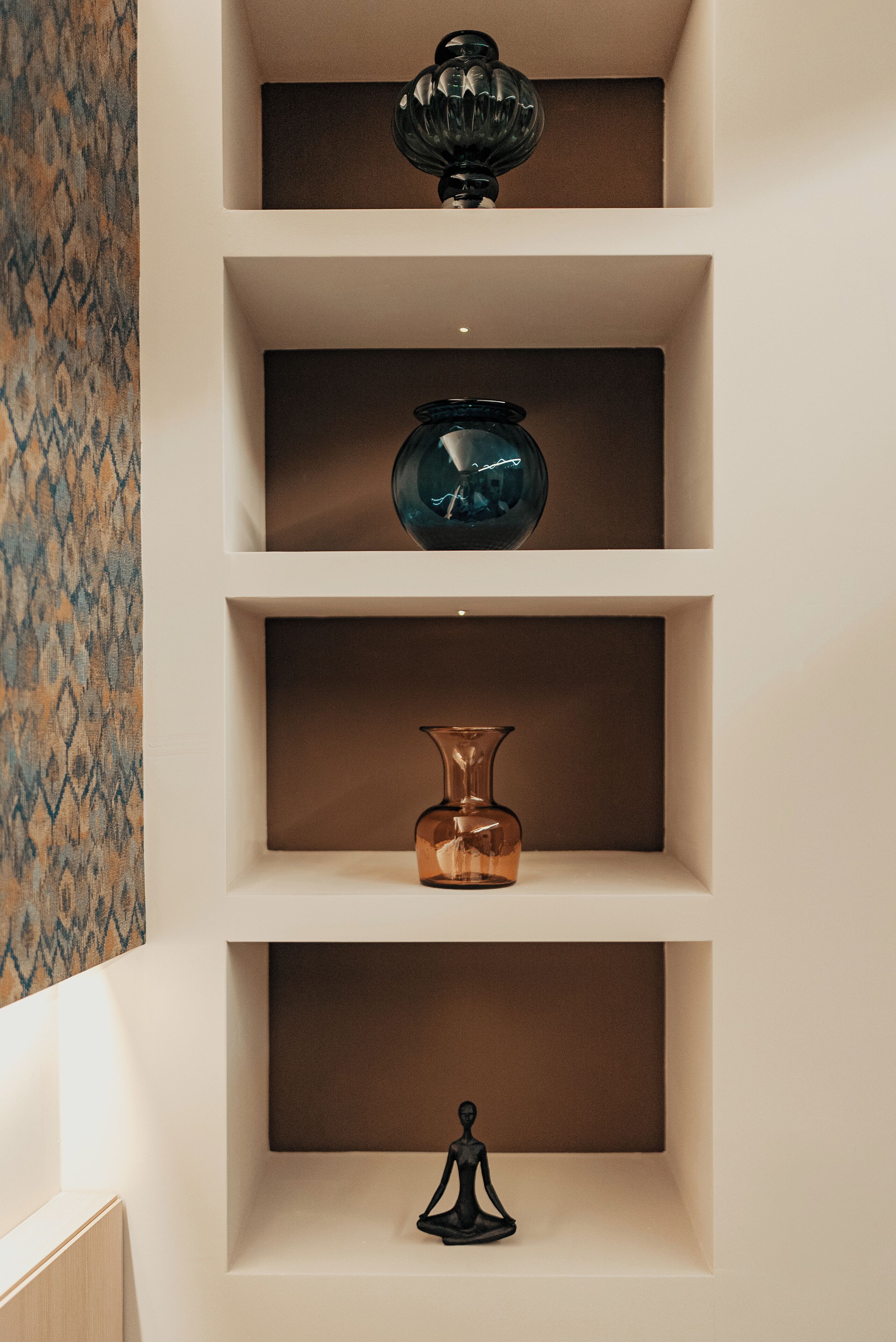 A wall-mounted shelf with three glass vases of different shapes and sizes.