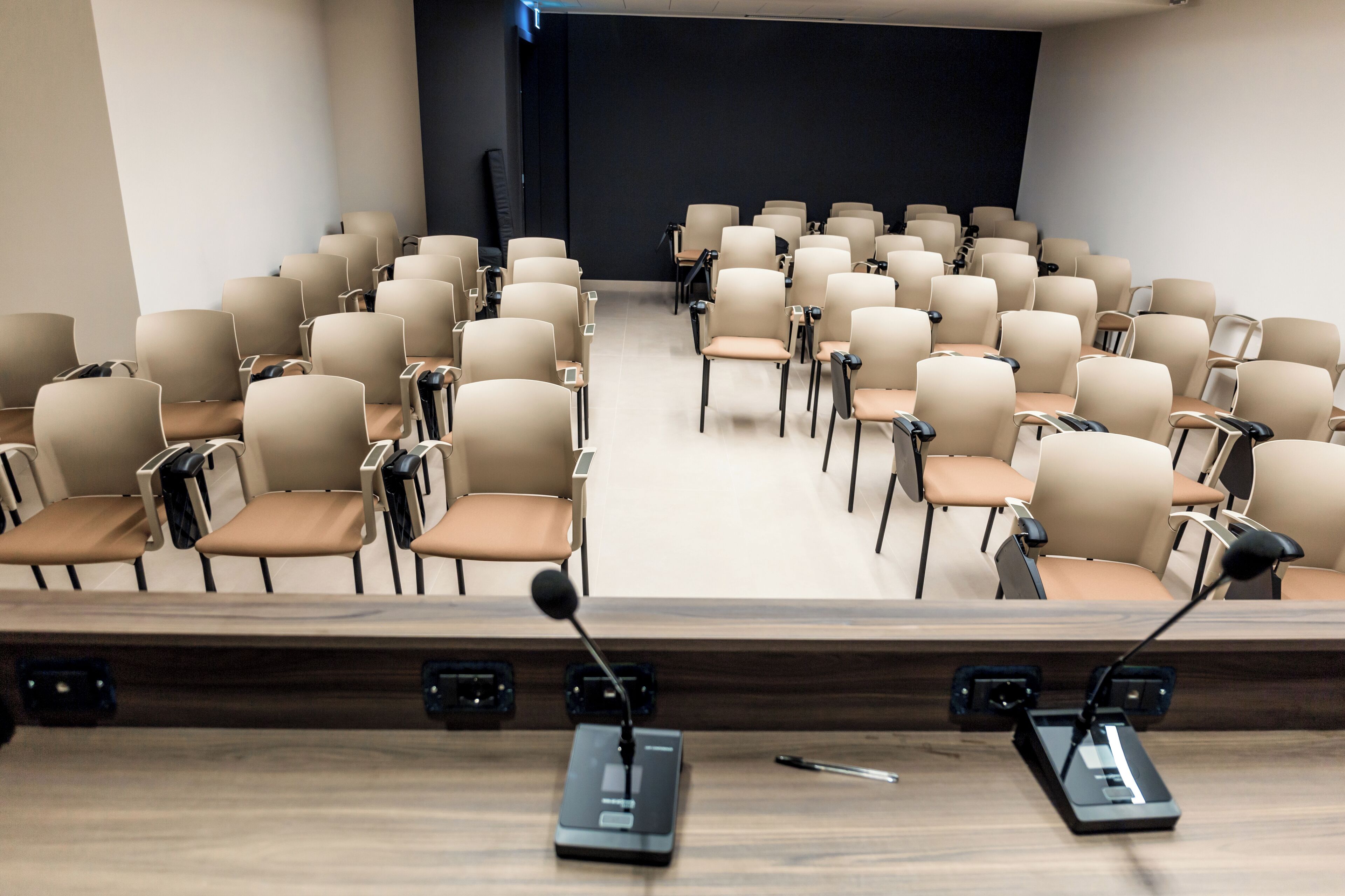 A conference room with rows of beige chairs, a podium with a microphone, and a projector screen.