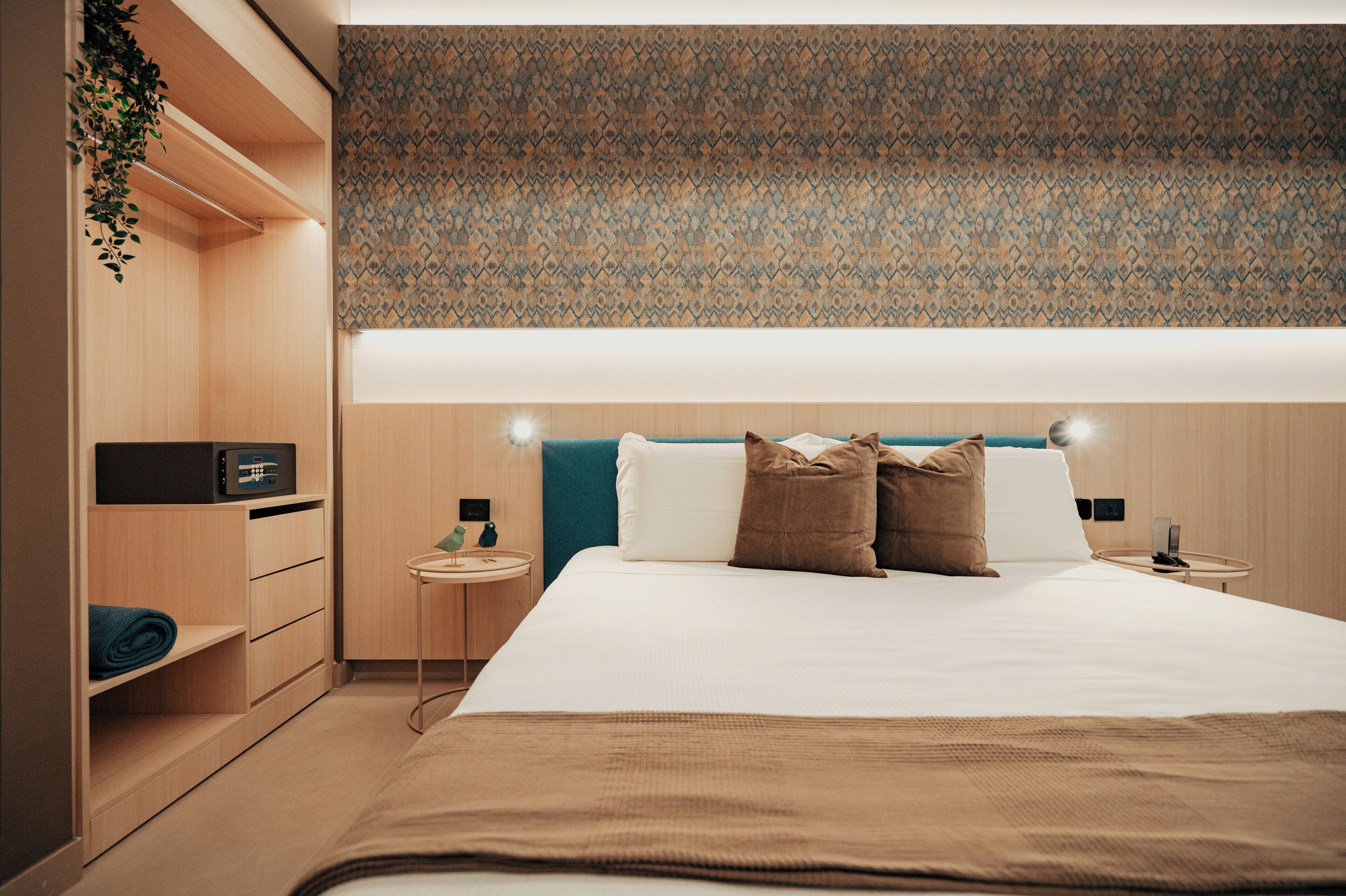 Une chambre d’hôtel moderne avec un grand lit, une armoire en bois, des tables de chevet et un mur décoré d’un motif.