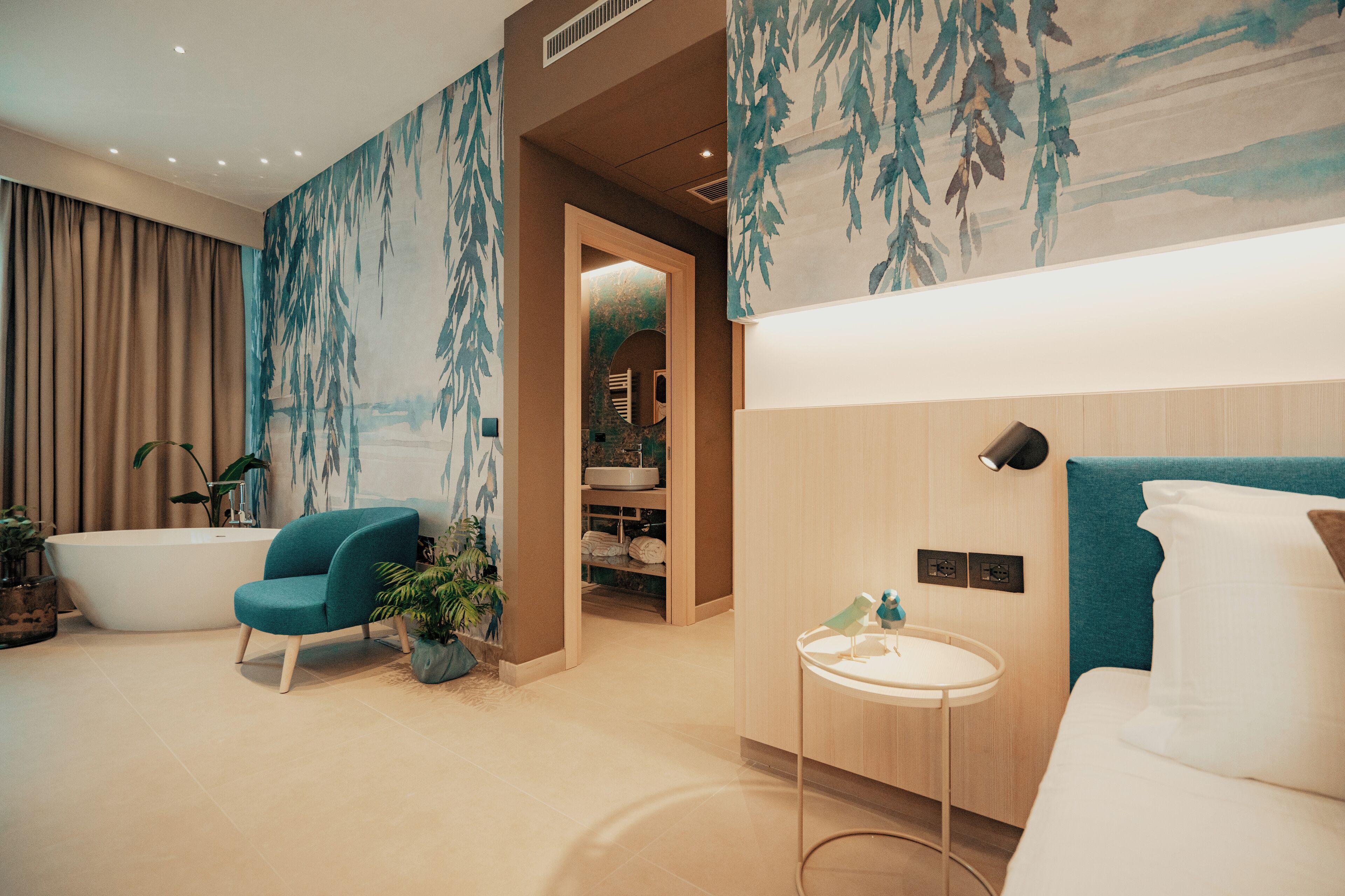 A modern bathroom with a bathtub, a sink, and a shower area. There is a chair and a small table with a lamp.