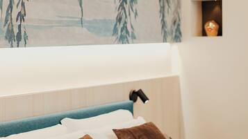 A bedroom with a bed, pillows, a nightstand, a lamp, and a wall with a hanging plant.