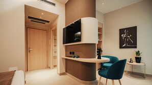 A modern room with a curved wall-mounted TV, a round table with a chair, a door, and a small side table with a plant.