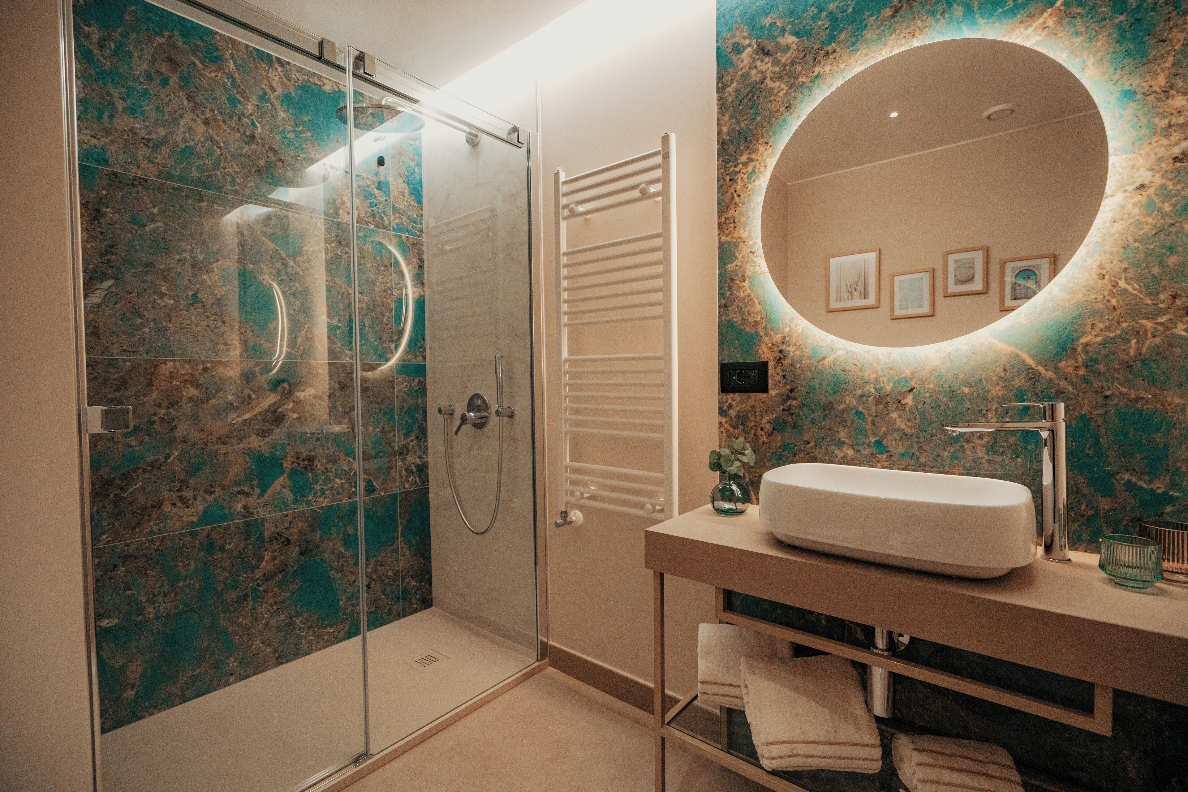 Um banheiro moderno com chuveiro em box de vidro, espelho redondo e painel de backsplash em mármore.