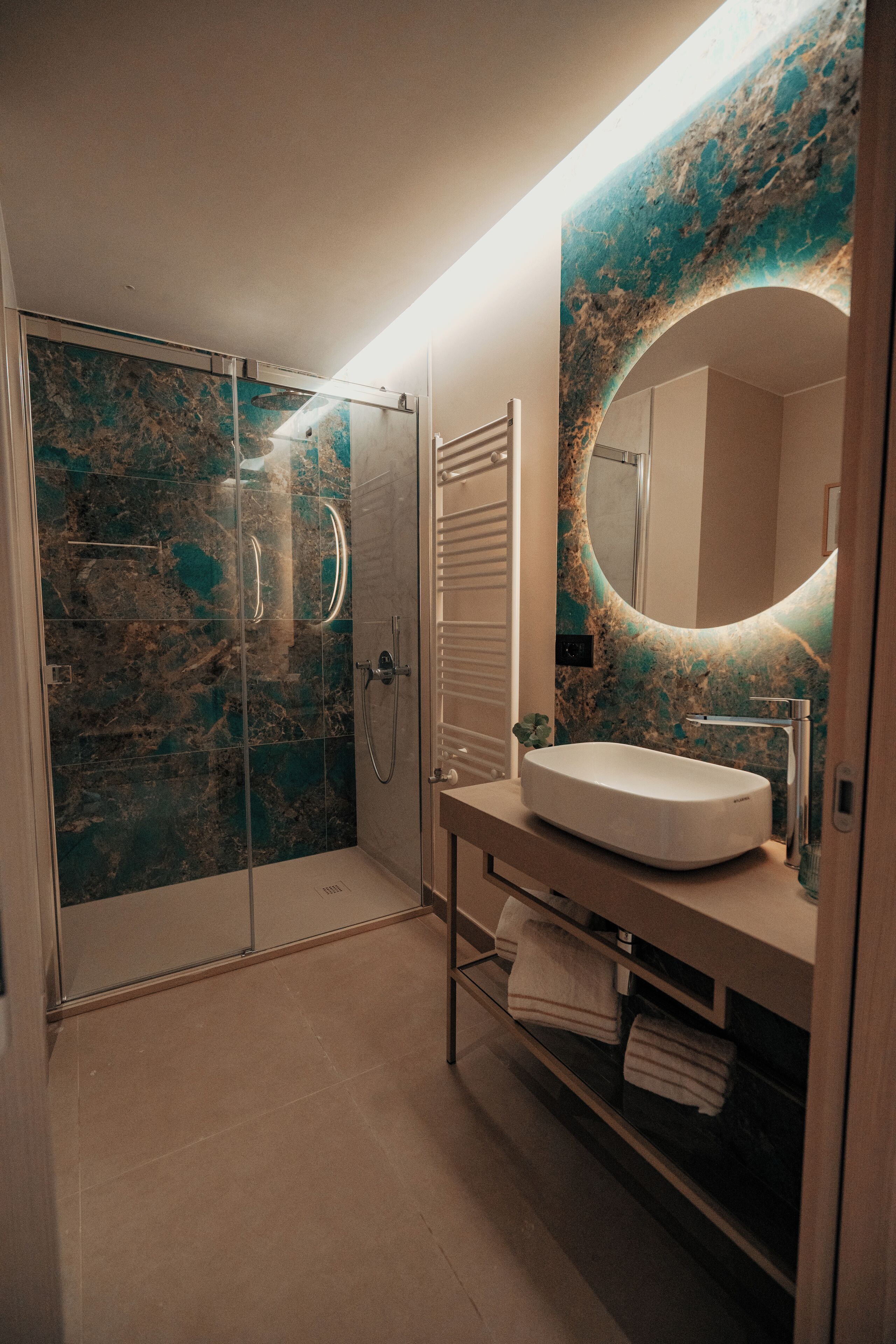 Un baño moderno con ducha de vidrio, salpicadero de mármol y un espejo grande con marco circular.