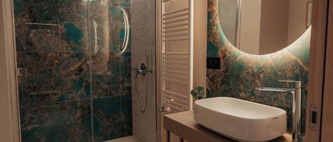 Un baño moderno con ducha de vidrio, salpicadero de mármol y un espejo grande con marco circular.