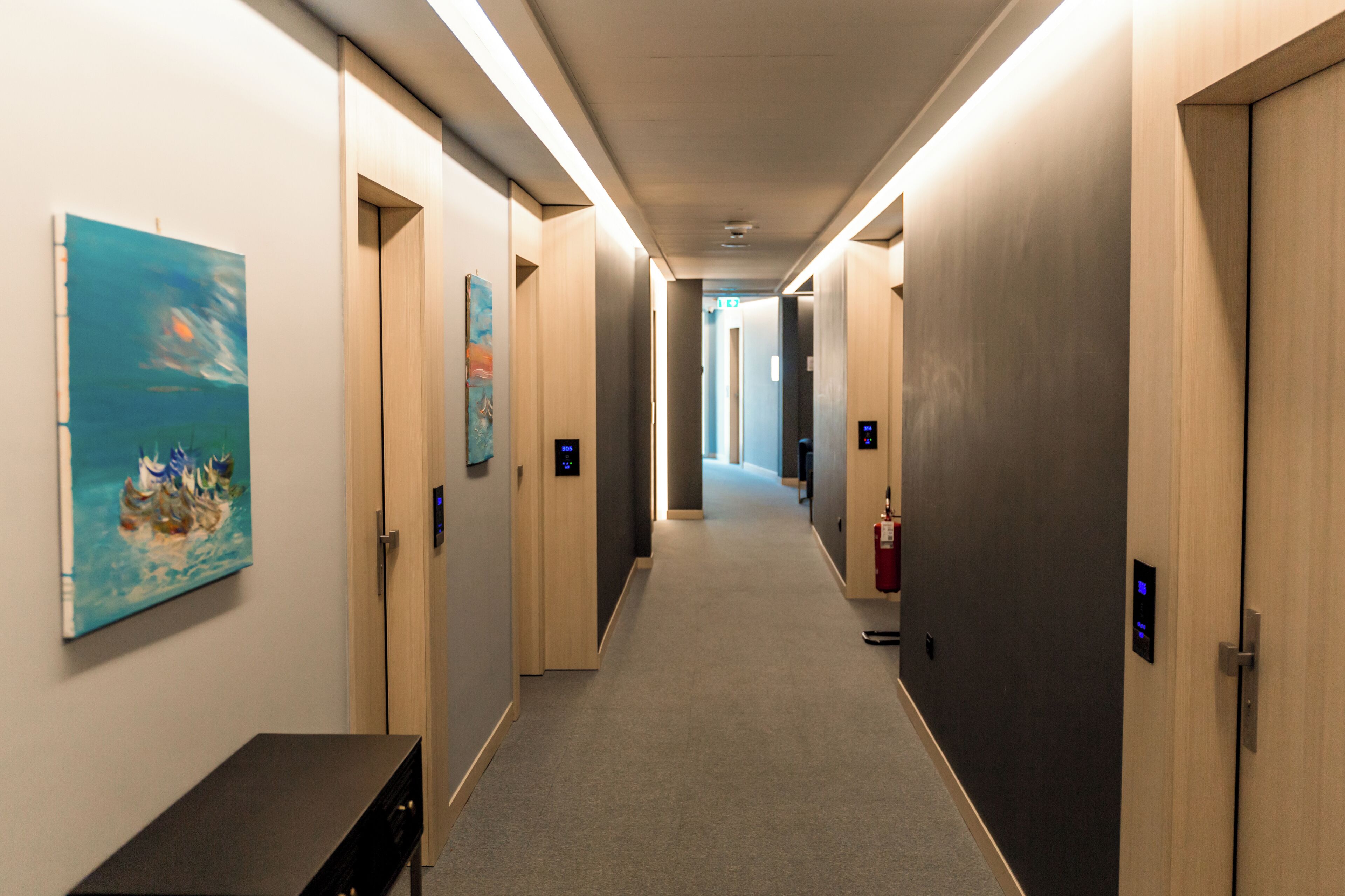 A hotel hallway with a carpeted floor, wooden doors, and artwork on the walls.