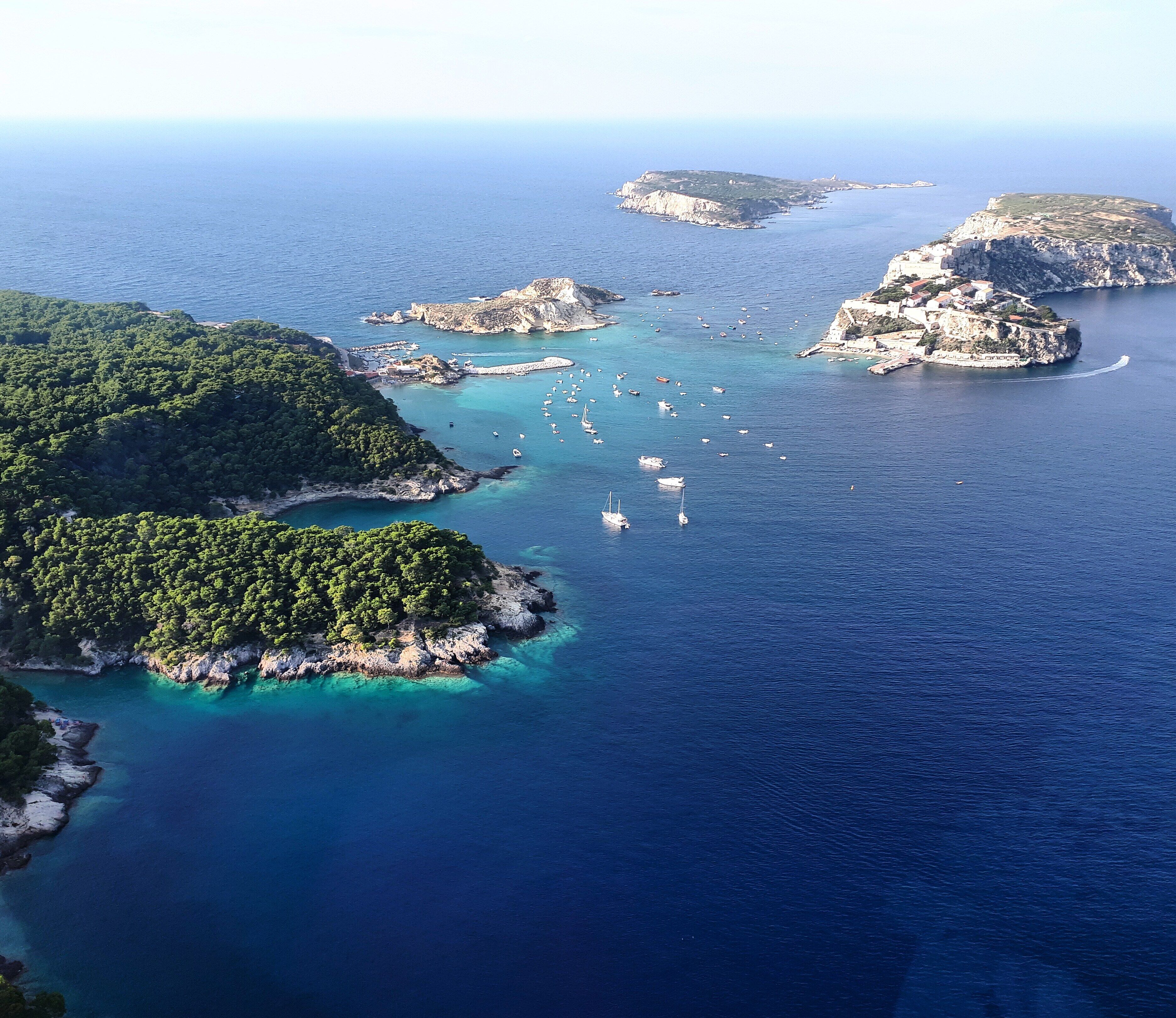 An aerial view of a coastal area with clear blue waters, rocky islands, and a marina with boats.