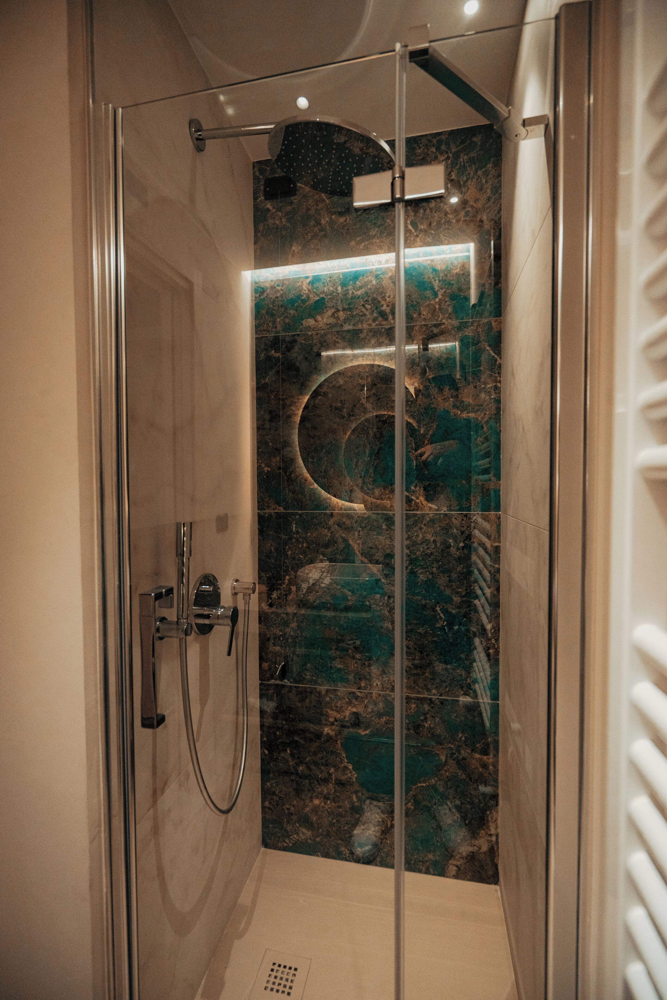 Una ducha moderna con puerta de cristal, pared de mármol y lavamanos empotrado.