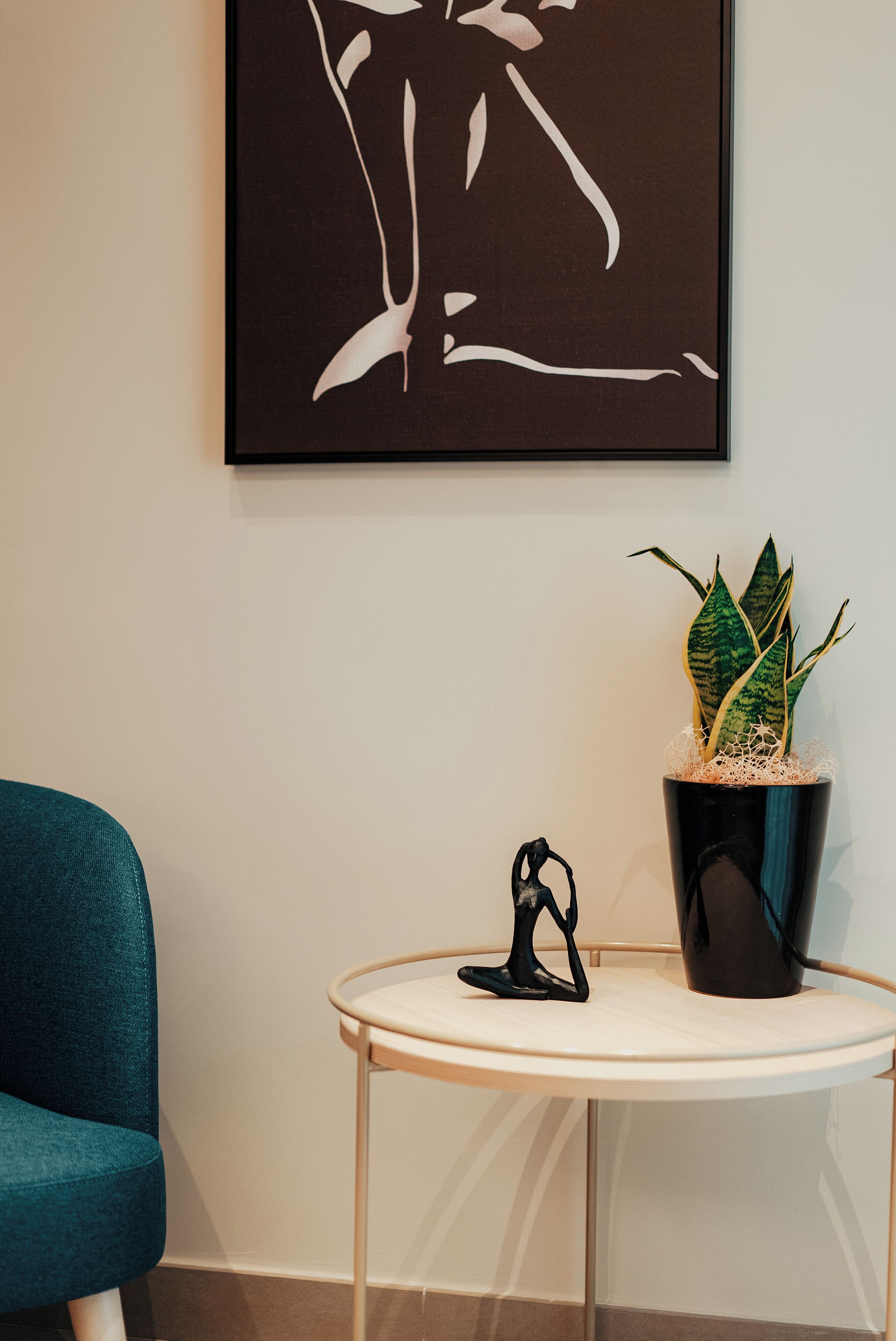 Una habitación con una silla color turquesa, una pequeña mesa redonda con una planta en maceta y una obra de arte enmarcada en la pared.