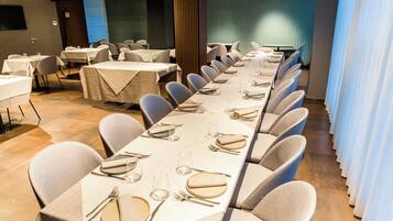Sala de conferências com mesas preparadas para uma reunião, equipada com cadeiras e mesas, e uma grande janela com cortinas.